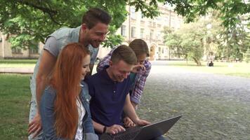 Four students share a joyful moment while laughing at a laptop on campus video