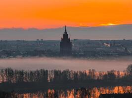 A vibrant sunrise over Riga, Latvia, with the Latvian Academy of Sciences in view, mist covered cityscape, and the Daugava River reflecting warm hues. photo