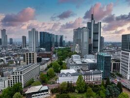 Aerial view of Frankfurt, Germany, featuring modern skyscrapers like the Commerzbank Tower, green spaces, and a sky with soft, colorful clouds. photo