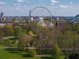 Aerial view of Riga Victory Park in Latvia, featuring a Ferris wheel, blooming sakura trees, green spaces, and the cityscape with the Latvian National Library. photo