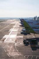 A busy airport tarmac with multiple airplanes, including a green and white Baltic aircraft. Ground vehicles, runway, and terminal buildings are visible. photo