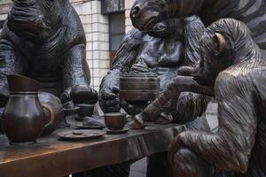 A detailed bronze sculpture of a chimpanzee, zebra, and rhinoceros at a tea party. Set in an urban London setting with a stone building in the background. photo