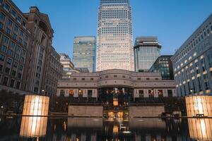 Twilight view of Canary Wharf in London featuring One Canada Square, modern office buildings, and a calm water feature reflecting the illuminated skyline. photo