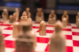 A detailed view of a chessboard with red and white squares, featuring intricately carved chess pieces resembling abstract handcrafted figures. photo