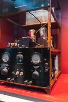 A historical radio transmitter with dials, gauges, and switches displayed on a red surface, featuring a wooden frame and labeled operational details. photo