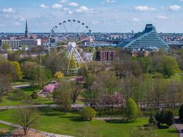 Riga Victory Park in Latvia features a Ferris wheel, blooming sakura trees, the National Library of Latvia, the cityscape, and the Daugava River. photo