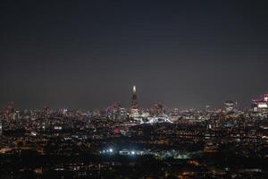 Illuminated Shard skyscraper at night with Tower Bridge spanning the River Thames. The London Eye is visible in the distance under a clear sky. photo