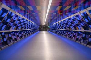 A modern pedestrian tunnel in London featuring a vibrant checkerboard pattern, soft blue lighting, and a symmetrical geometric design leading to a glass exit. photo