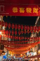 A vibrant street in London's Chinatown at night, featuring red lanterns with Chinese characters, a golden text banner, illuminated storefronts, and a lively crowd. photo
