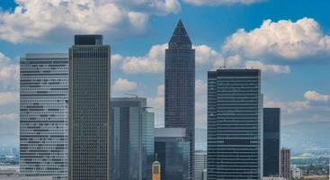 Frankfurt's skyline features the Messeturm with its pyramid roof, modern high rises like the Trianon, a church with a golden cross, and a cloudy sky. photo