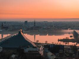Serene sunrise view of Riga, Latvia, featuring the Daugava River, the National Library's angular design, and historic church spires in the background. photo