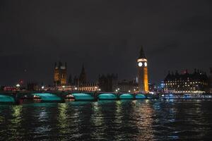 Illuminated Big Ben and Houses of Parliament at night with Westminster Bridge spanning the River Thames, green lights reflecting on the water. photo