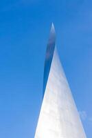 A sleek metallic structure with a sharp, tapering point and reflective surface set against a clear blue sky, showcasing modern architectural design. photo