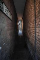Narrow alleyway named Catherine Wheel Alley in London, flanked by aged brick walls. A faint light fixture adds a subtle glow to the dim corridor. photo