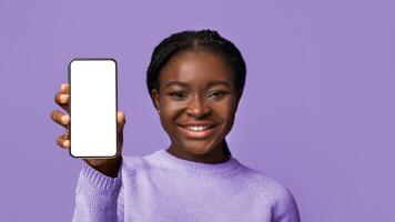 Great App. Mockup image of modern smartphone with black blank screen in hands of beautiful african american woman isolated on purple background, template for your design, selective focus, copy space photo