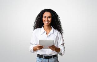 Curly Brunette Woman Posing With Digital Tablet In Hands Over Yellow Background In Studio, Smiling At Camera, Copy Space photo
