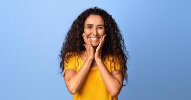 Joyful Brunette Woman Touching Face In Happy Excitement And Looking At Camera, Smiling Millennial Lady Standing Pleasantly Surprised, Having Fun Over Purple Studio Background, Copy Space photo