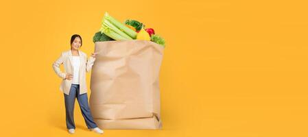A customer stands beside a large paper bag overflowing with fresh produce, showcasing a vibrant collection of vegetables. The background is bright and cheerful, reflecting the joy of shopping. photo