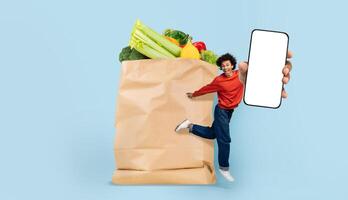 A person joyfully holds a smartphone next to a large paper bag filled with fresh vegetables and fruits. This captures the essence of modern grocery shopping and delivery. photo