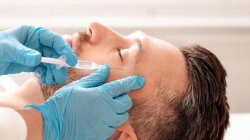 Cosmetologist making eye lifting procedures for handsome middle aged man at aesthetic clinic, side view. Man getting beauty injection against eye wrinkles from unrecognizable plastic surgeon photo