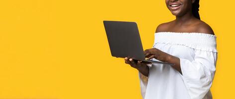 Cheerful Black Woman Posing With Laptop In Hands Over Yellow Studio Background, Working Remotely, Doing Online Business, Checking New Website, Browsing Social Media And Smiling At Camera, Copy Space photo