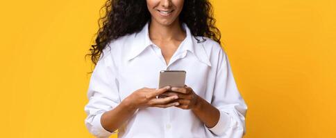 Stylish Brunette Woman Using Smartphone Over Yellow Background In Studio, Messaging With Friends Or Browsing Internet, Young Lady Holding Cellphone, Enjoying Modern Technologies, Copy Space photo