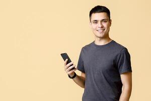 Modern guy student blogger typing message to blog followers. Friendly confident young man in casual with smart watch hold phone and look at camera, isolated on light sand background, empty space photo