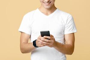 Modern communication, chat in social networks and mobile app. Cheerful cute young guy student with glasses typing on mobile smartphone in blog, isolated on beige background, studio shot, free space photo
