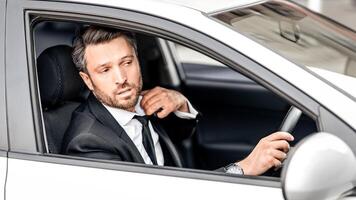 Stressed middle-aged businessman driving car, lowering his tie, getting late for his flight, side view, shot from car window, copy space. Nervous entrepreneur stuck in traffic on a way to airport photo