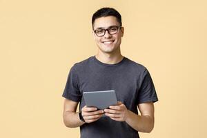Handsome student blogger works at home on self-isolation. Cheerful young man in glasses with smart watch holds digital tablet and read blog or surfing on internet, isolated on light background photo