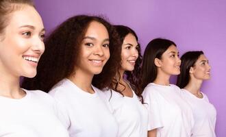 Group Of Cheerful Multicultural Ladies Posing Together Standing In A Row Over Purple Background. Diversity, Female Unity And Equality Concept. Studio Shot, Selective Focus photo