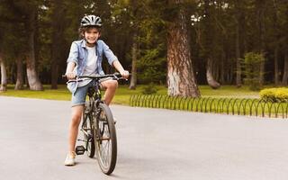Urban Lifestyle. Smiling curly boy standing on a bicycle in park and posing, looking at camera, copy space photo