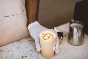 Drink from professional barista and most delicious espresso. African american barista in apron gives to client cup of coffee with drawing in interior of modern cafe, top view, empty space, cropped photo