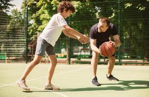 Training. Portrait in motion of mature guy teaching small boy how to play basketball photo