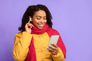 Black Woman With Mobile Phone And Earbuds Making Call Or Listening To Music Online In Earphones Standing Over Blue Studio Background. Gadget, Distant Communication Concept. Free Space photo