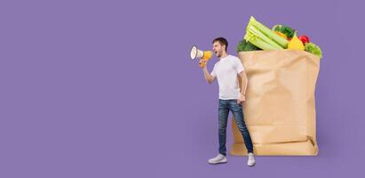 A customer stands beside a large paper grocery bag filled with fresh produce. He is holding a megaphone and appears to be making an announcement about shopping. photo