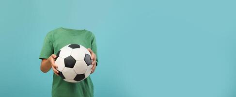 A child stands holding a soccer ball, but their head is missing in this minimalist setup. The vibrant background adds focus to the playful activity of sports and fun. photo