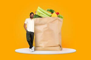 A satisfied customer stands beside a large paper bag filled with fresh fruits and vegetables. This reflects the new normal of grocery shopping from home and convenient delivery options. photo