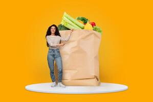 A customer stands with a large paper bag filled with fresh vegetables and fruits. The backdrop is bright yellow, emphasizing the emphasis on wholesome grocery shopping at home. photo