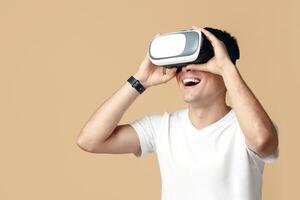 Virtual gadgets for entertainment, work, free time and study. Surprised happy guy student in white t-shirt uses vr glasses and looks at empty space, isolated on light background, studio shot photo