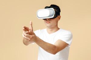 Modern entertainment, online games and technology for fun. Serious young student man in virtual reality glasses shoots with hand from imaginary pistol, isolated on light background, empty space photo