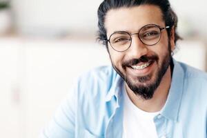 Closeup Portrait Of Positive Arab Guy With Dental Braces And Eyeglasses Smiling At Camera, Handsome Bearded Millennial Man With Brackets On Teeth Posing Indoors, Selective Focus With Copy Space photo