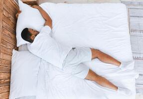 Unrecognizable Black Guy Sleeping Lying On Stomach In Bed At Home. African Man Resting And Relaxing Napping In His Bedroom. Recreation And Rest Concept. View From Above photo