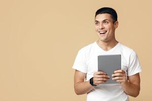 Great ad, offer and amazing news from blogger. Surprised happy european young man student with open mouth holding digital tablet and look at free space, isolated on beige background, studio shot photo