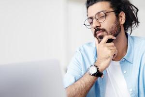 Closeup Portrait Of Focused Handsome Arab Guy In Eyeglasses Working On Laptop, Looking At Computer Screen With Pensive Face Expression, Eastern Man Ckecking Information In Internet, Free Space photo