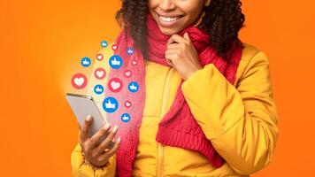 Unrecognizable Black Lady Using Cellphone Networking Chatting In Social Media, Commenting And Texting In Mobile App Posing Over Yellow Studio Background. Collage With Like Buttons And Hearts, Cropped photo