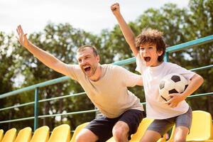 Win Concept. Happy family of two watching soccer game on playing field, screaming and celebrating victory photo