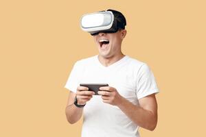 Virtual gadgets for entertainment, work, free time and study. Surprised happy man student in white t-shirt uses vr glasses and smartphone, isolated on light background, studio shot photo