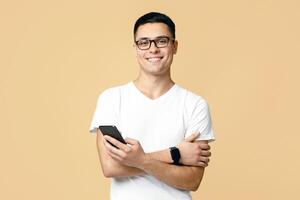 Social media, app, modern communication. Attractive cute zoomer student in glasses, white t-shirt with smart watch hold smartphone and texting message, isolated on light sand background photo