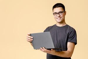 Freelance and work online at home in self-isolation. Happy young handsome man with glasses hold laptop and surfing in internet, isolated on light background, empty space photo